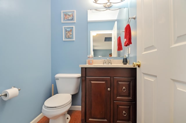 half bathroom with an inviting chandelier, vanity, toilet, wood finished floors, and baseboards