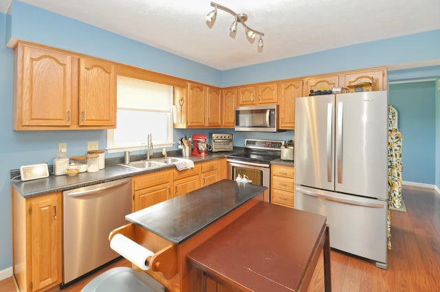 kitchen with a kitchen island, appliances with stainless steel finishes, wood finished floors, a sink, and dark countertops
