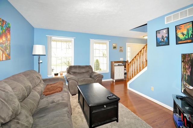 living room with visible vents, baseboards, wood finished floors, and stairs
