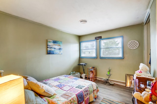 bedroom featuring a baseboard heating unit, visible vents, and wood finished floors