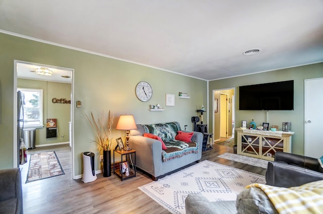 living area with baseboards, wood finished floors, visible vents, and crown molding