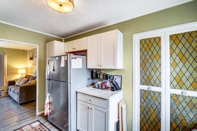 kitchen featuring white cabinets, wood finished floors, freestanding refrigerator, light stone countertops, and crown molding