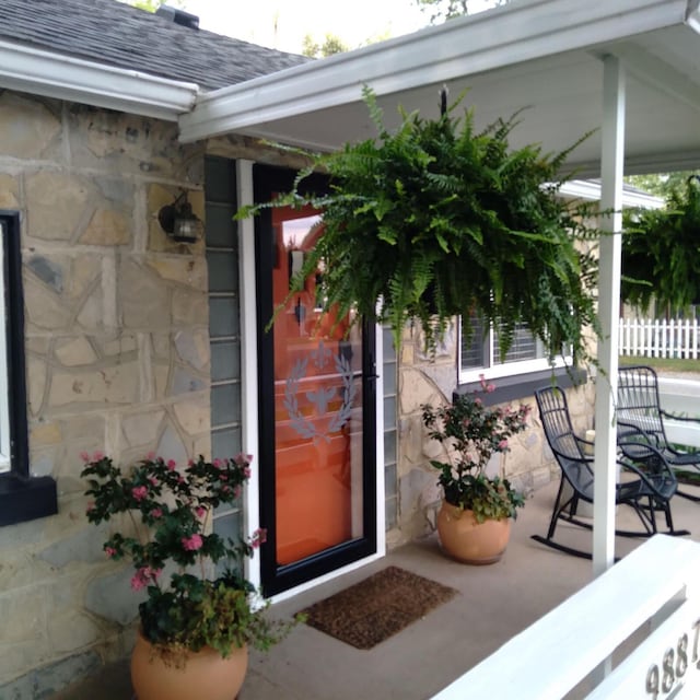 entrance to property featuring covered porch, a shingled roof, and stone siding