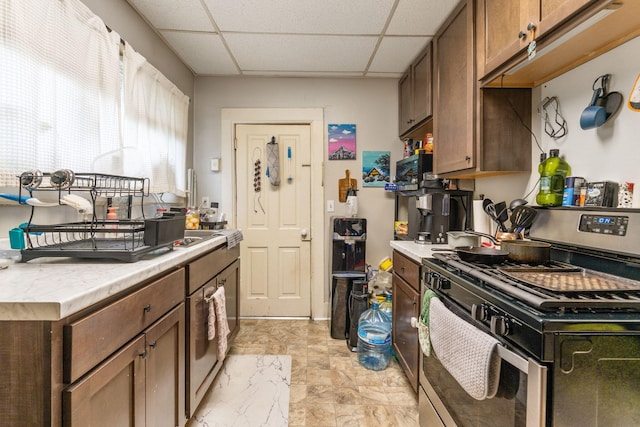 kitchen featuring a paneled ceiling, stainless steel range with gas stovetop, and light countertops