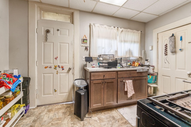 kitchen featuring a paneled ceiling, brown cabinets, light countertops, and gas stove