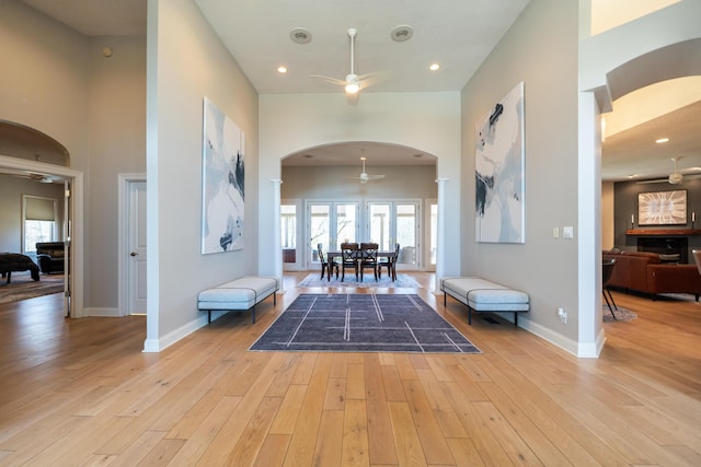 foyer featuring baseboards, arched walkways, light wood finished floors, and ceiling fan