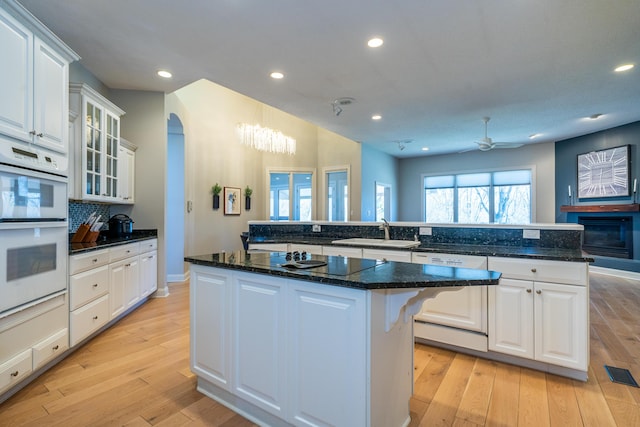 kitchen featuring a sink, a kitchen island, arched walkways, dishwashing machine, and white double oven