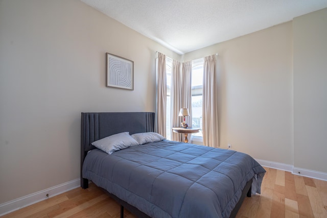 bedroom featuring baseboards, a textured ceiling, and light wood-style flooring