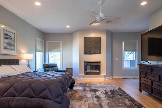 bedroom with a glass covered fireplace, multiple windows, light wood-style floors, and recessed lighting