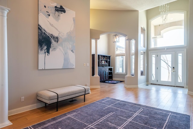 foyer entrance featuring wood finished floors, a high ceiling, baseboards, and decorative columns