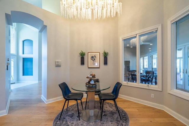 dining room with light wood-type flooring, baseboards, arched walkways, and an inviting chandelier