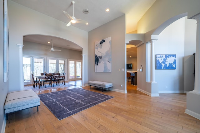 living area with light wood-type flooring, decorative columns, arched walkways, and ceiling fan