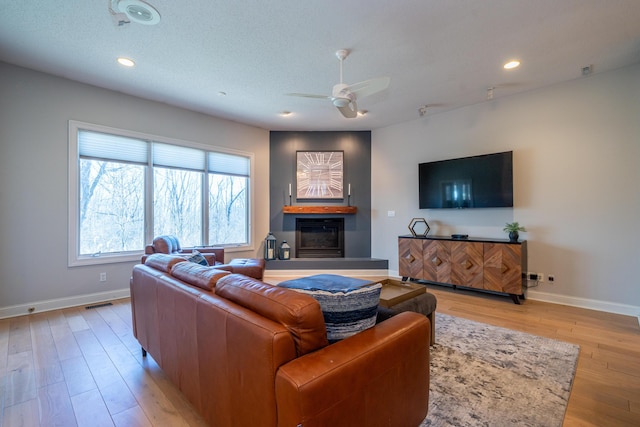 living area with recessed lighting, a glass covered fireplace, light wood-style flooring, and baseboards