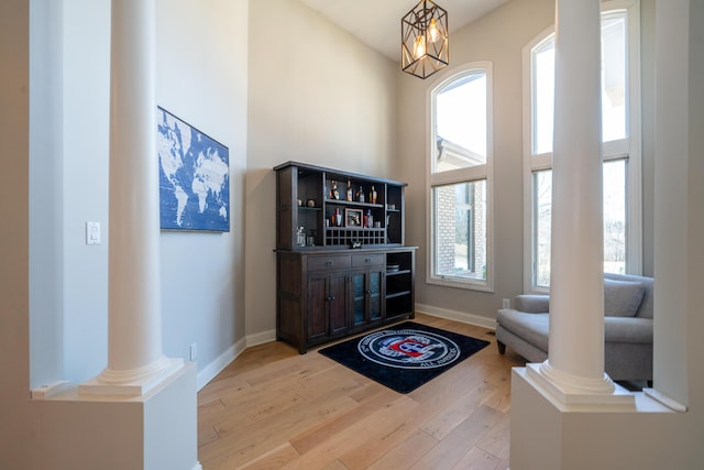 foyer entrance featuring light wood-style flooring, decorative columns, baseboards, and a towering ceiling