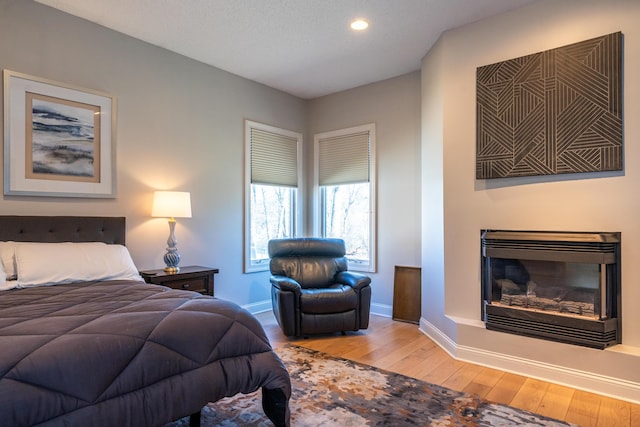 bedroom with a glass covered fireplace, hardwood / wood-style flooring, recessed lighting, and baseboards