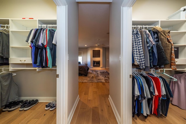 walk in closet featuring a fireplace with raised hearth, hardwood / wood-style floors, and a ceiling fan