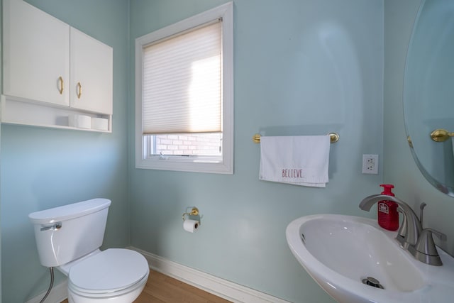 half bath with toilet, wood finished floors, baseboards, and a sink