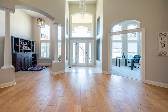 entrance foyer featuring wood finished floors, baseboards, ornate columns, a high ceiling, and arched walkways