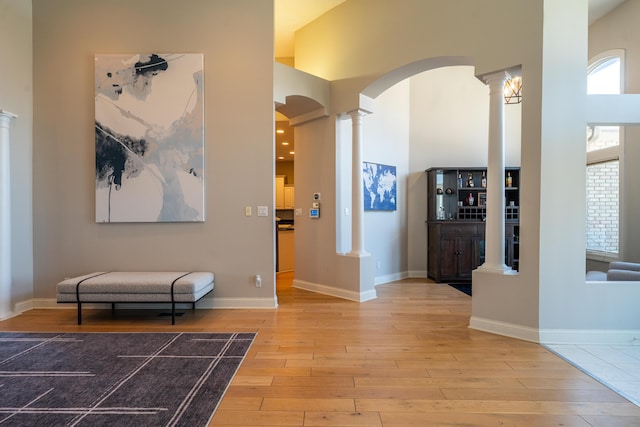 corridor with wood finished floors, baseboards, ornate columns, arched walkways, and a towering ceiling