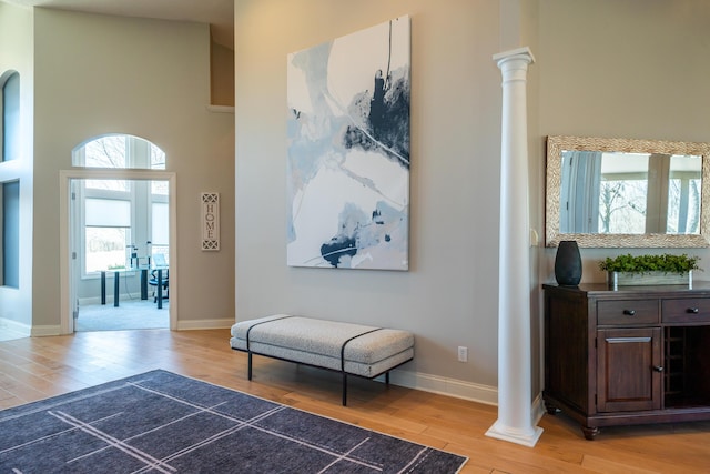 hall with a towering ceiling, light wood-style floors, baseboards, and ornate columns