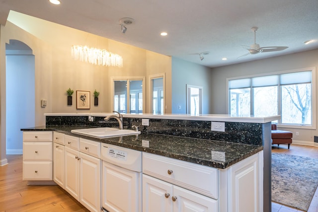 kitchen with dishwasher, dark stone counters, light wood-type flooring, arched walkways, and a sink