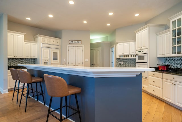 kitchen with light wood-style flooring, recessed lighting, a breakfast bar area, white cabinets, and glass insert cabinets