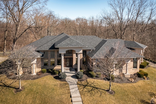 view of front facade with a front yard, brick siding, and a shingled roof