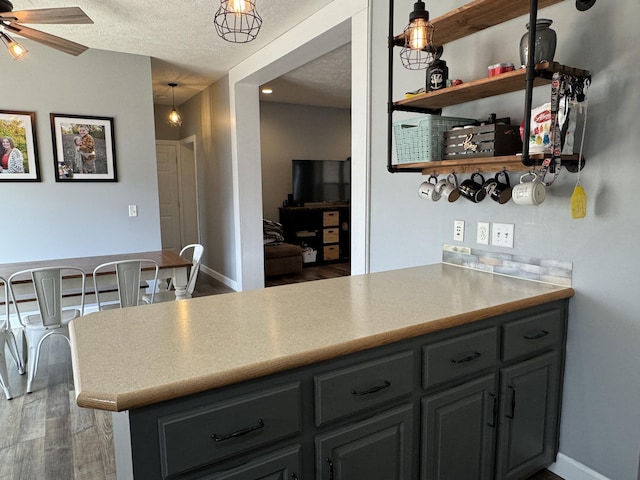 kitchen with hanging light fixtures, a textured ceiling, dark hardwood / wood-style flooring, kitchen peninsula, and ceiling fan