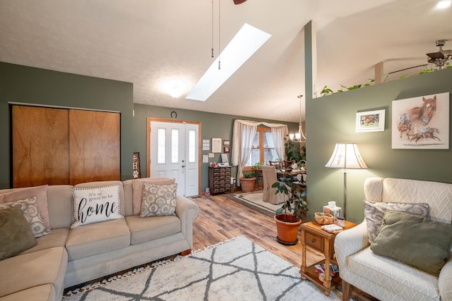 living room featuring hardwood / wood-style floors, vaulted ceiling with skylight, and ceiling fan with notable chandelier