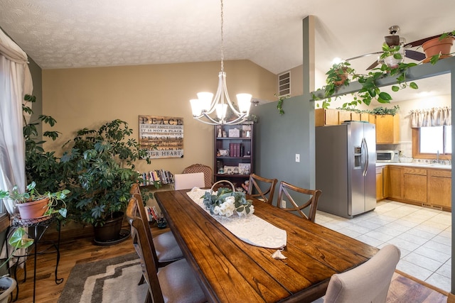 tiled dining room featuring lofted ceiling, ceiling fan with notable chandelier, and a textured ceiling