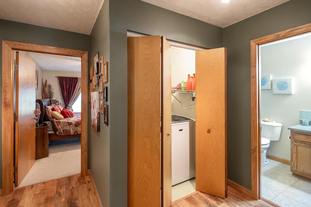 corridor featuring washer / clothes dryer, a textured ceiling, and light wood-type flooring