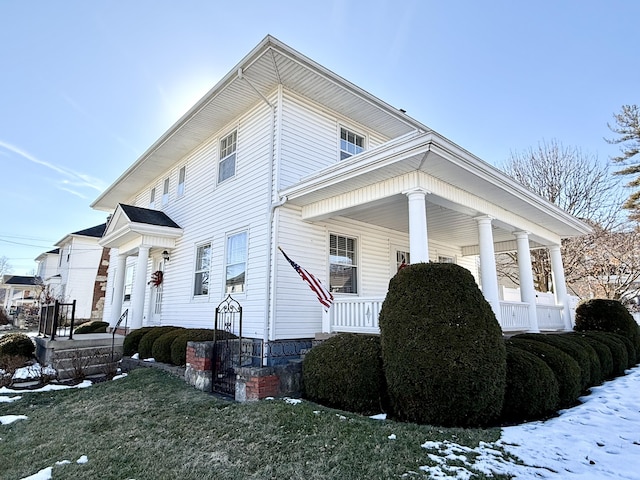 view of snow covered exterior featuring a porch and a lawn