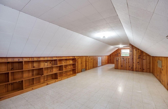 bonus room with built in features, vaulted ceiling, wood walls, and light floors