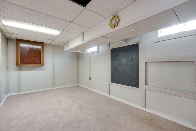 basement featuring a drop ceiling, carpet flooring, and baseboards