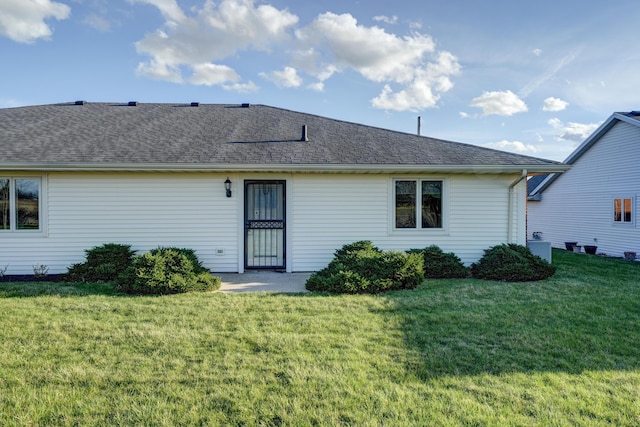 rear view of house featuring a shingled roof and a lawn