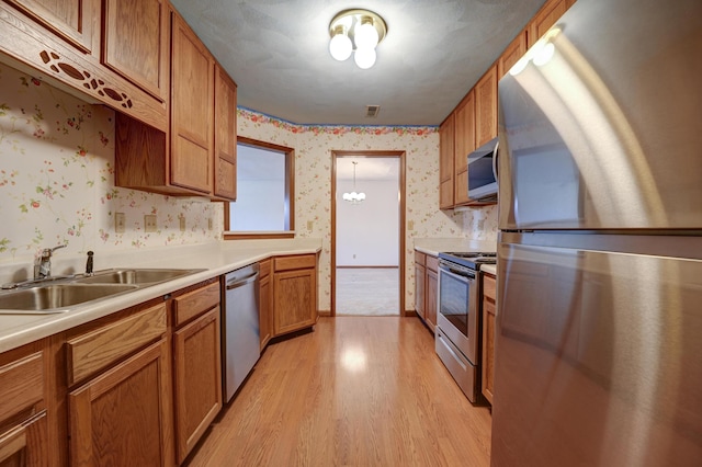 kitchen featuring wallpapered walls, a sink, light wood-style floors, appliances with stainless steel finishes, and brown cabinetry