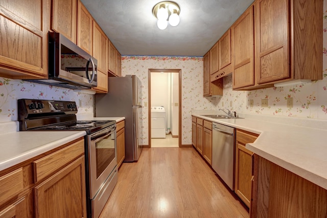 kitchen featuring a sink, wallpapered walls, washer / dryer, and stainless steel appliances