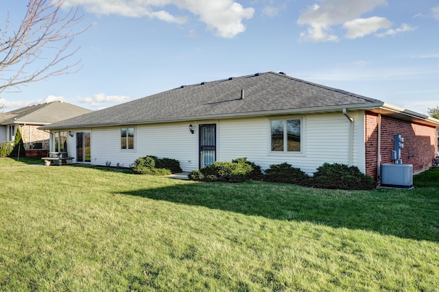 rear view of property featuring brick siding, a shingled roof, and a yard