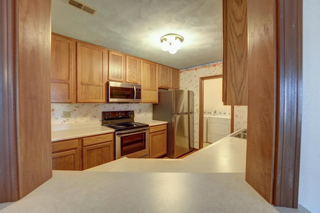 kitchen with light countertops, washing machine and clothes dryer, wallpapered walls, visible vents, and appliances with stainless steel finishes