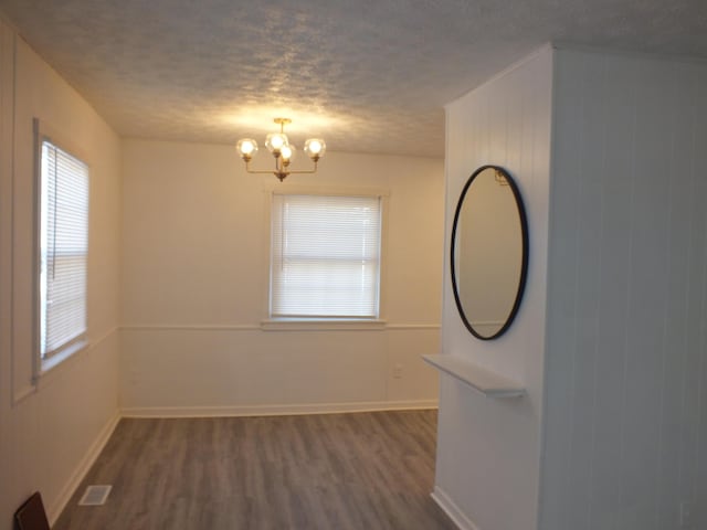 empty room with a textured ceiling, dark wood-type flooring, and a chandelier