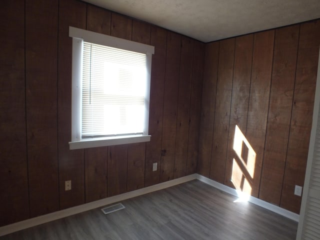 unfurnished room with dark hardwood / wood-style floors, a textured ceiling, and wood walls