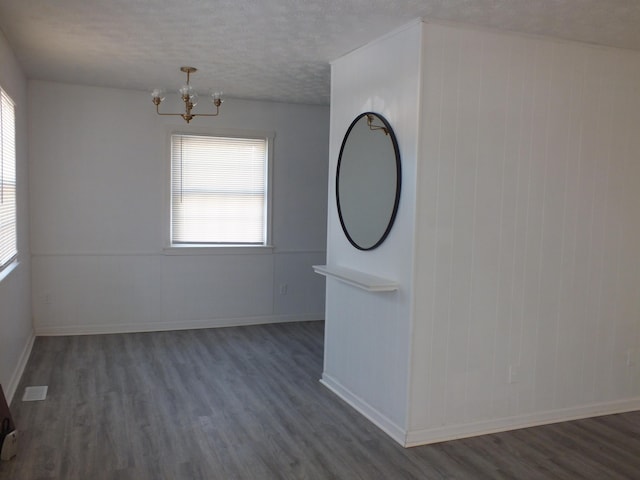 empty room with an inviting chandelier, dark hardwood / wood-style flooring, and a textured ceiling