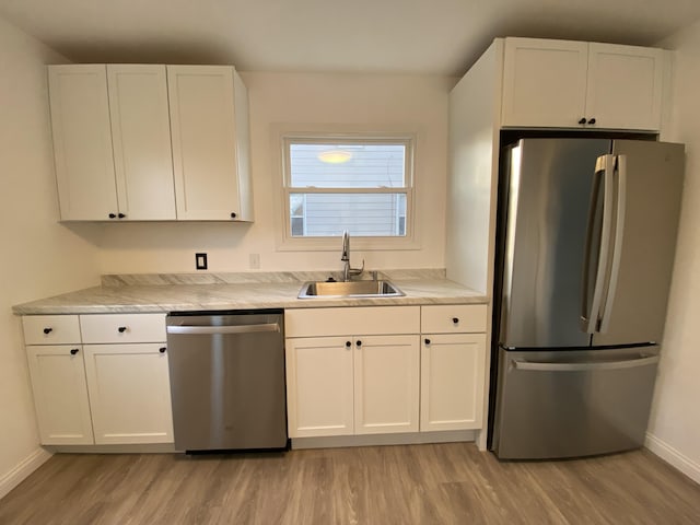 kitchen with white cabinetry, stainless steel appliances, sink, and light hardwood / wood-style flooring