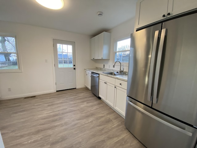 kitchen with stainless steel appliances, white cabinetry, light stone countertops, and sink