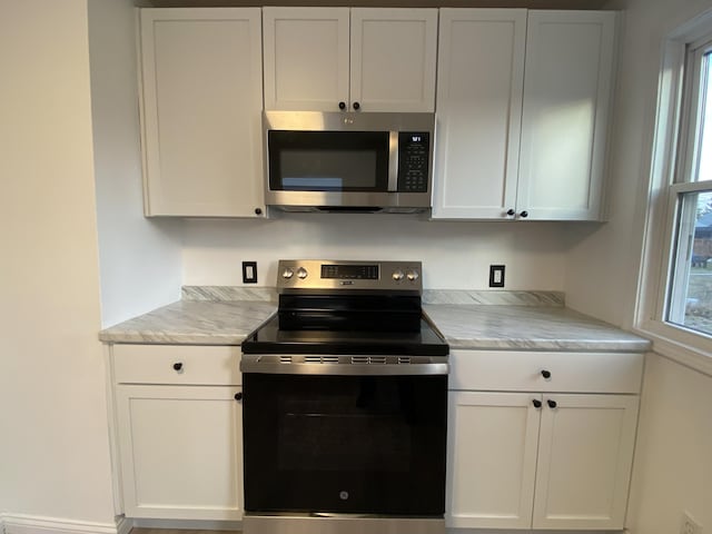 kitchen with white cabinetry, light stone counters, and appliances with stainless steel finishes