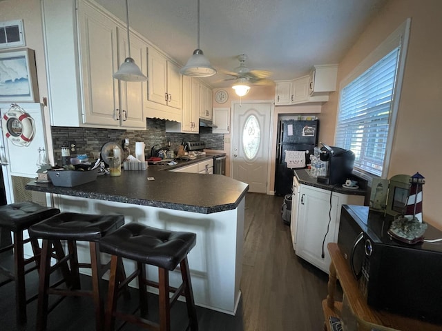 kitchen featuring stainless steel electric stove, dark countertops, decorative backsplash, white cabinetry, and a peninsula