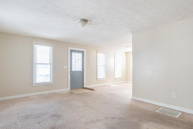 spare room with light colored carpet, visible vents, a textured ceiling, and baseboards