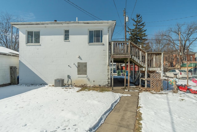 snow covered property featuring central air condition unit, stairs, and fence