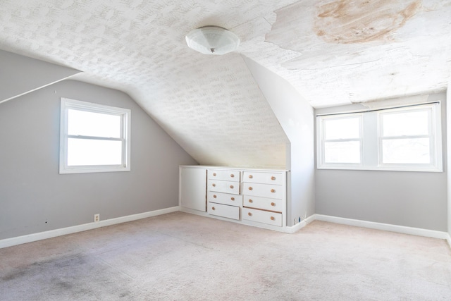 additional living space with a textured ceiling, vaulted ceiling, light carpet, and baseboards