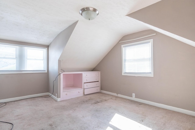 additional living space featuring light carpet, vaulted ceiling, a textured ceiling, and baseboards